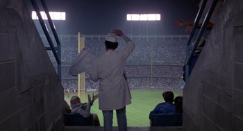 Movie still from “52 Pick-Up” (1986), directed by John Frankenheimer – A man in a baseball uniform saluting at a baseball game; Wide shot, Low angle