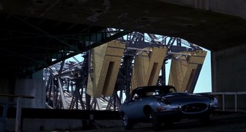 Movie still from “52 Pick-Up” (1986), directed by John Frankenheimer – A car is parked under a bridge in a city; Wide shot, Low angle