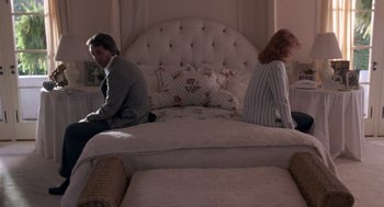 Movie still from “52 Pick-Up” (1986), directed by John Frankenheimer – A man and a woman sitting back to back on a bed; Wide shot, High angle