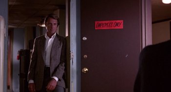 Movie still from “52 Pick-Up” (1986), directed by John Frankenheimer – A man standing in front of an entrance to an office building; Medium shot, Low angle