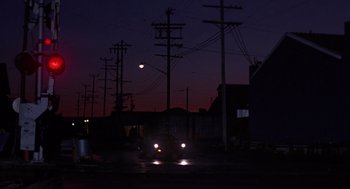 Movie still from “52 Pick-Up” (1986), directed by John Frankenheimer – A car driving down a street at night with lights on; Extreme Wide shot, Low angle