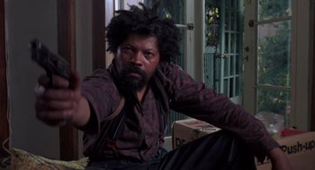 Movie still from “52 Pick-Up” (1986), directed by John Frankenheimer – A man sitting on a chair with a beard; Medium shot, Low angle