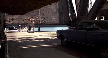 Movie still from “52 Pick-Up” (1986), directed by John Frankenheimer – Two people standing next to an old blue car; Wide shot, High angle