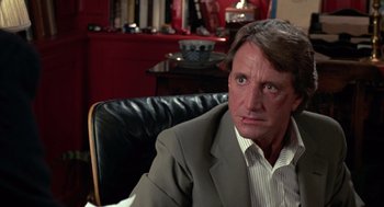 Movie still from “52 Pick-Up” (1986), directed by John Frankenheimer – A person sitting in a chair wearing a suit; Close Up shot, Over the shoulder angle