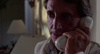 Movie still from “52 Pick-Up” (1986), directed by John Frankenheimer – An older man talking on a phone while wearing a suit; Close Up shot, Low angle