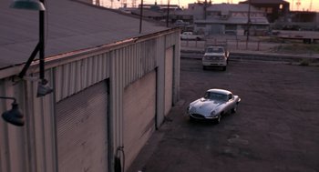 Movie still from “52 Pick-Up” (1986), directed by John Frankenheimer – An old car parked in a parking lot next to a building; Extreme Wide shot, High angle