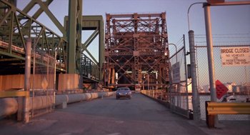 Movie still from “52 Pick-Up” (1986), directed by John Frankenheimer – A car is driving on a bridge over a river; Extreme Wide shot, High angle