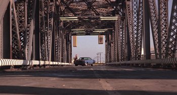 Movie still from “52 Pick-Up” (1986), directed by John Frankenheimer – A car driving under a bridge with a person on it; Extreme Wide shot, Low angle