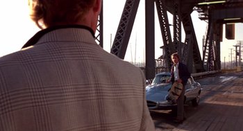 Movie still from “52 Pick-Up” (1986), directed by John Frankenheimer – A man standing next to a car on a bridge; Wide shot, Over the shoulder angle
