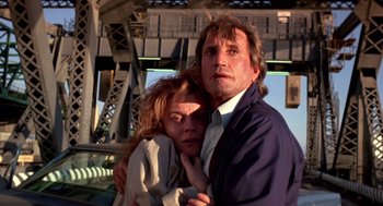 Movie still from “52 Pick-Up” (1986), directed by John Frankenheimer – A man and a woman hugging in front of a bridge; Close Up shot, Low angle