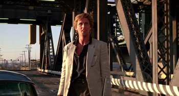 Movie still from “52 Pick-Up” (1986), directed by John Frankenheimer – A man in a suit standing in front of a bridge; Medium shot, Low angle