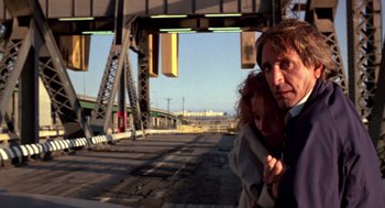Movie still from “52 Pick-Up” (1986), directed by John Frankenheimer – A man and a woman standing next to each other on the side of a road; Close Up shot, Low angle