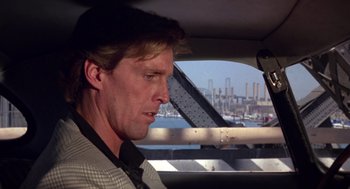 Movie still from “52 Pick-Up” (1986), directed by John Frankenheimer – A person in a car near a body of water; Close Up shot, Over the shoulder angle