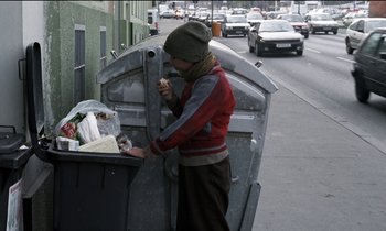 Movie still from “71 Fragments of a Chronology of Chance” (1994), directed by Michael Haneke – A man standing next to a garbage can on the side of the street; Wide shot, Low angle