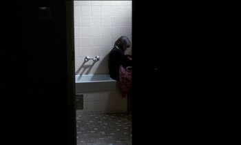 Movie still from “71 Fragments of a Chronology of Chance” (1994), directed by Michael Haneke – A woman sitting on a bathtub in a bathroom; Wide shot, High angle