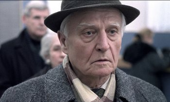 Movie still from “71 Fragments of a Chronology of Chance” (1994), directed by Michael Haneke – An older man wearing a hat and a jacket; Close Up shot, Over the shoulder angle