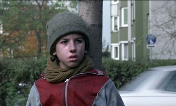 Movie still from “71 Fragments of a Chronology of Chance” (1994), directed by Michael Haneke – A young man wearing a hat and scarf; Medium shot, Low angle