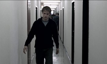 Movie still from “71 Fragments of a Chronology of Chance” (1994), directed by Michael Haneke – A man walking down a long hallway in a building; Medium shot, Low angle