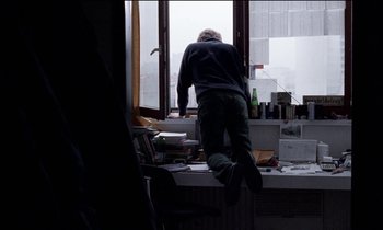 Movie still from “71 Fragments of a Chronology of Chance” (1994), directed by Michael Haneke – A man standing in front of a large window; Wide shot, High angle