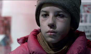 Movie still from “71 Fragments of a Chronology of Chance” (1994), directed by Michael Haneke – A young boy wearing a pink jacket and a gray hat; Close Up shot, Low angle
