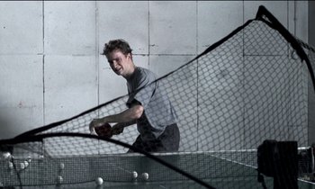 Movie still from “71 Fragments of a Chronology of Chance” (1994), directed by Michael Haneke – A man is playing ping pong on a tennis court; Medium shot, Low angle