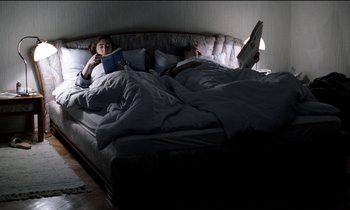 Movie still from “71 Fragments of a Chronology of Chance” (1994), directed by Michael Haneke – A person laying on a bed reading a book; Wide shot, High angle