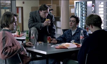 Movie still from “71 Fragments of a Chronology of Chance” (1994), directed by Michael Haneke – A group of people sitting at a table with drinks; Medium shot, Over the shoulder angle
