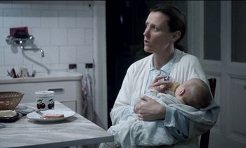 Movie still from “71 Fragments of a Chronology of Chance” (1994), directed by Michael Haneke – A woman sitting at a table with a baby; Close Up shot, Over the shoulder angle