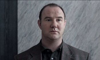 Movie still from “71 Fragments of a Chronology of Chance” (1994), directed by Michael Haneke – A person wearing a suit and tie; Close Up shot, Low angle