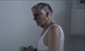 Movie still from “71 Fragments of a Chronology of Chance” (1994), directed by Michael Haneke – An older man in a white tank top holding a towel; Medium shot, Over the shoulder angle