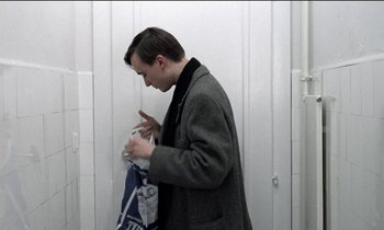 Movie still from “71 Fragments of a Chronology of Chance” (1994), directed by Michael Haneke – A man in a gray coat is holding a bag; Medium shot, Over the shoulder angle