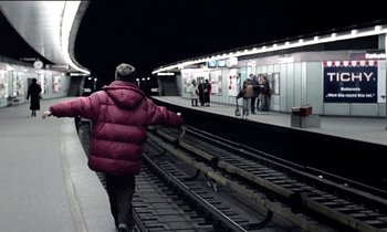 Movie still from “71 Fragments of a Chronology of Chance” (1994), directed by Michael Haneke – A person walking on a train track next to a platform; Wide shot, Low angle