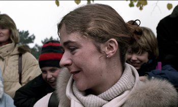 Movie still from “71 Fragments of a Chronology of Chance” (1994), directed by Michael Haneke – A young woman with a white scarf and a bunch of other young people; Close Up shot, Over the shoulder angle