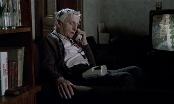 Movie still from “71 Fragments of a Chronology of Chance” (1994), directed by Michael Haneke – An older man sitting on a couch talking on a phone; Medium shot, High angle