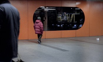 Movie still from “71 Fragments of a Chronology of Chance” (1994), directed by Michael Haneke – A man in a red jacket walking in a train station; Wide shot, Over the shoulder angle