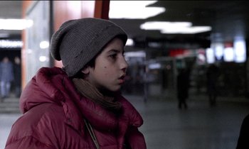 Movie still from “71 Fragments of a Chronology of Chance” (1994), directed by Michael Haneke – A boy in a red jacket and a gray hat; Close Up shot, Over the shoulder angle