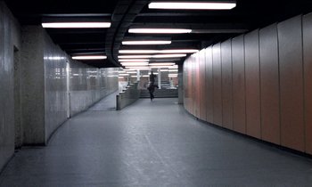 Movie still from “71 Fragments of a Chronology of Chance” (1994), directed by Michael Haneke – A person is walking down a walkway in a building; Extreme Wide shot, High angle