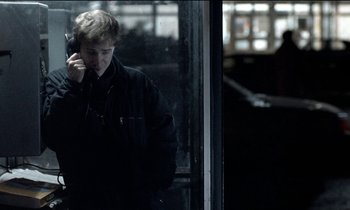 Movie still from “71 Fragments of a Chronology of Chance” (1994), directed by Michael Haneke – A man talking on a cell phone while standing in front of a window; Medium shot, Over the shoulder angle
