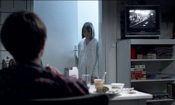 Movie still from “71 Fragments of a Chronology of Chance” (1994), directed by Michael Haneke – A young girl standing in front of a television; Medium shot, Over the shoulder angle