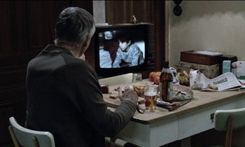 Movie still from “71 Fragments of a Chronology of Chance” (1994), directed by Michael Haneke – A man sitting in front of a television; Medium shot, High angle
