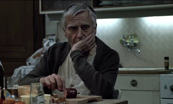 Movie still from “71 Fragments of a Chronology of Chance” (1994), directed by Michael Haneke – An older man sitting at a table with an apple in front of him; Close Up shot, Over the shoulder angle