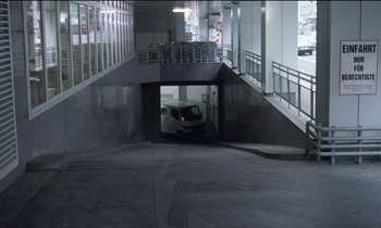 Movie still from “71 Fragments of a Chronology of Chance” (1994), directed by Michael Haneke – A car is parked in a parking garage under an overpass; Extreme Wide shot, High angle