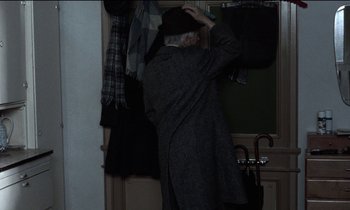 Movie still from “71 Fragments of a Chronology of Chance” (1994), directed by Michael Haneke – An older man in a hat and coat hanging clothes on a rack; Medium shot, Over the shoulder angle