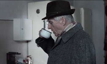 Movie still from “71 Fragments of a Chronology of Chance” (1994), directed by Michael Haneke – An older man drinking a cup of coffee; Medium shot, Over the shoulder angle