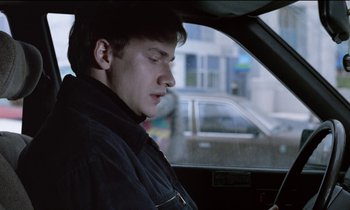 Movie still from “71 Fragments of a Chronology of Chance” (1994), directed by Michael Haneke – A man sitting in the driver's seat of a car looking at his cell phone; Close Up shot, Low angle