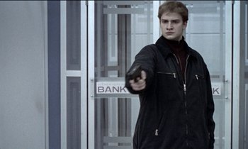 Movie still from “71 Fragments of a Chronology of Chance” (1994), directed by Michael Haneke – A young man holding a gun in front of a bank sign; Medium shot, Low angle