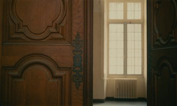 Movie still from “7 Rm., kit., ba...” (1984), directed by Agnès Varda – A door and window in a room with sunlight coming through the window; Medium shot, Low angle