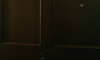 Movie still from “7 Rm., kit., ba...” (1984), directed by Agnès Varda – A dark room with a door and a window; Close Up shot, Low angle