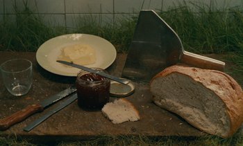 Movie still from “7 Rm., kit., ba...” (1984), directed by Agnès Varda – Bread , butter , and jam on a cutting board; Extreme Close Up shot, Overhead angle