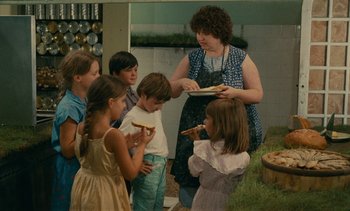 Movie still from “7 Rm., kit., ba...” (1984), directed by Agnès Varda – A group of children eating pizza in a kitchen; Medium shot, High angle